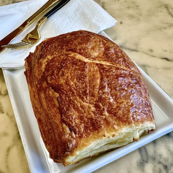Golden-brown pastry on a white rectangular plate with gold cutlery and a white napkin.