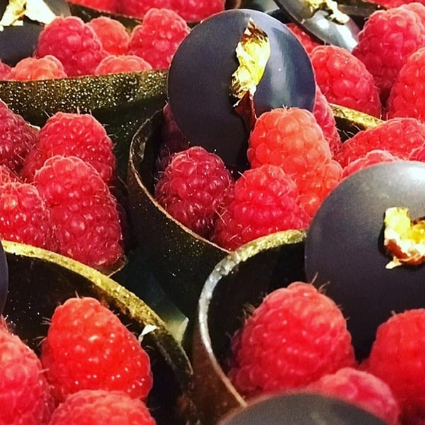 Close-up of fresh raspberries nestled in dark chocolate cups with gold leaf accents.