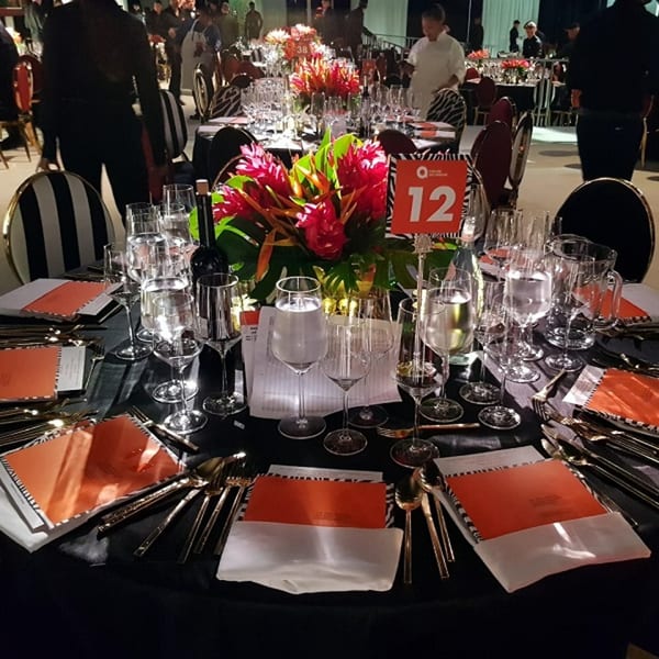 Elegantly set dining table with red floral centerpiece, wine glasses, and orange place settings.