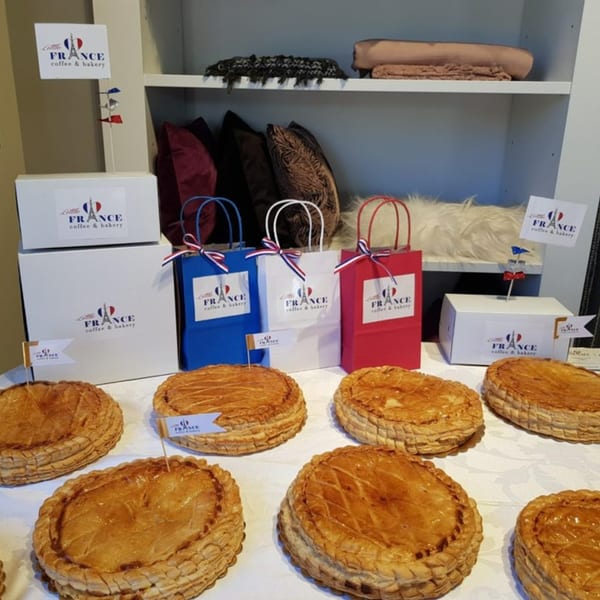 Golden-brown Galette des Rois pastries on a white tablecloth with Little France Coffee & Bakery branded packaging.