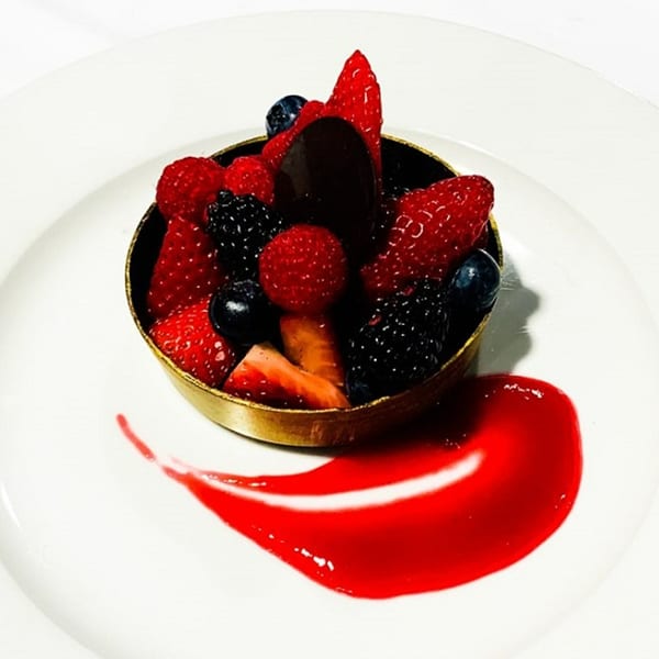 A golden tart shell filled with fresh strawberries, raspberries, blueberries, and blackberries, with a red sauce swirl.
