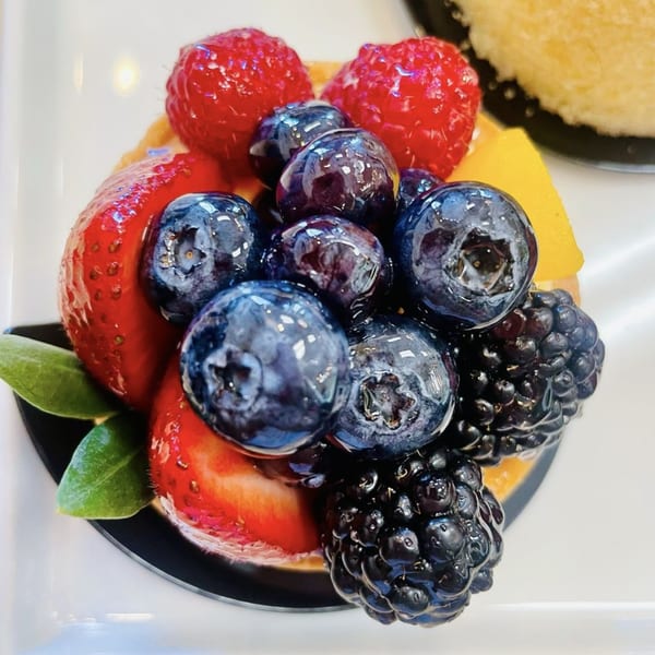 A close-up of a berry tart from Little France Coffee & Bakery, topped with glistening blueberries, raspberries, and blackberries.