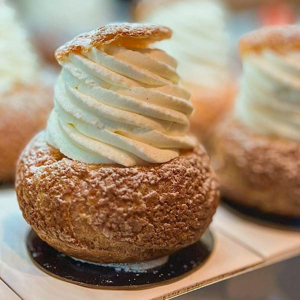 A choux pastry puff with a swirl of white cream and powdered sugar on top.