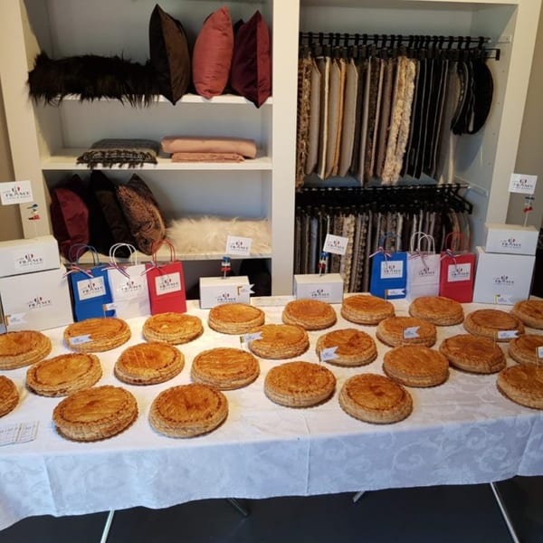 A table laden with golden-brown Galette des Rois pastries, gift bags, and boxes from Little France Coffee & Bakery.