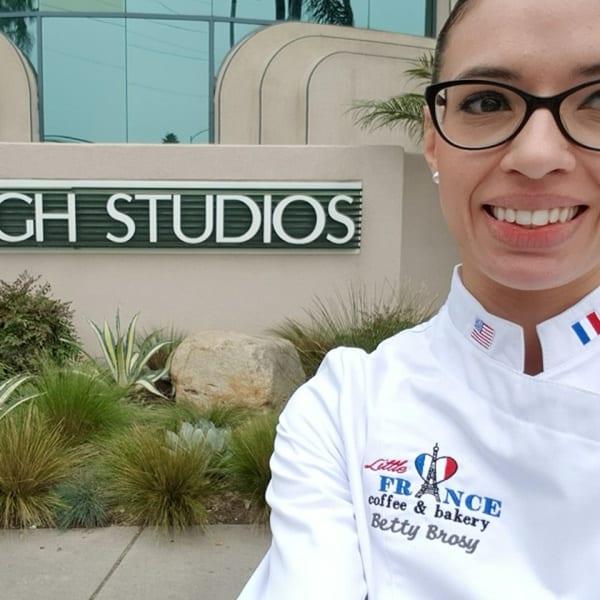 Betty Brosy, owner of Little France Coffee & Bakery, smiling in front of "CH STUDIOS" sign.