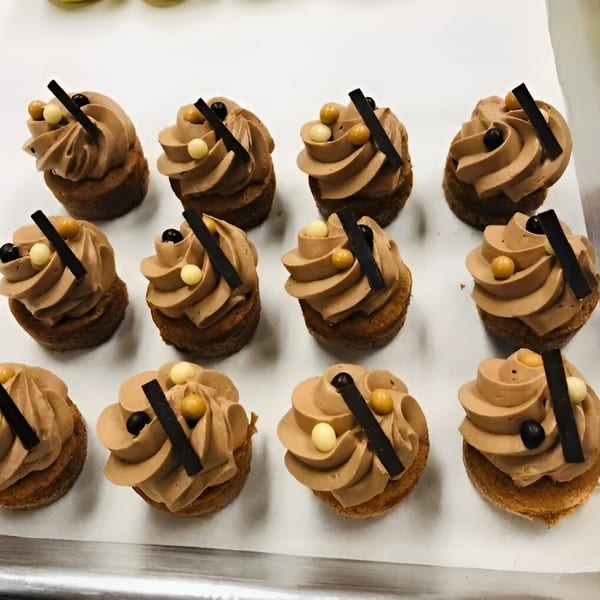 Twelve mini chocolate tarts with piped frosting, chocolate sticks, and candy pearls on a white tray.