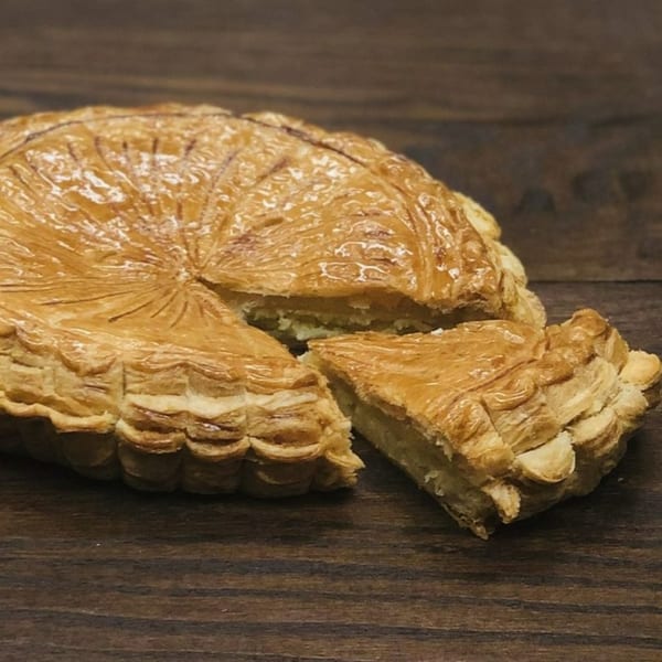 A golden-brown Galette des Rois with a slice cut out, revealing its creamy filling.
