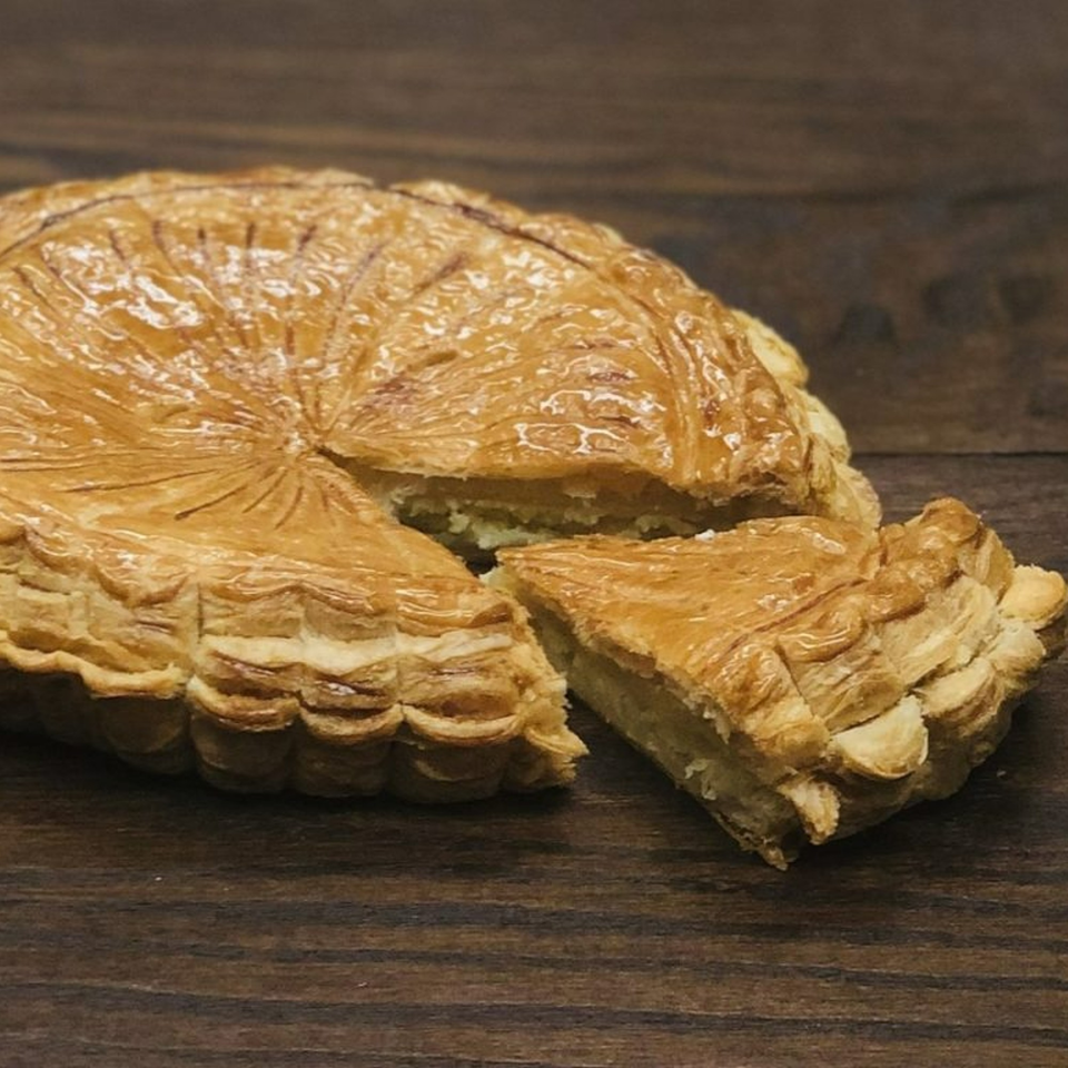 A golden-brown Galette des Rois with a slice cut out, revealing its creamy filling.